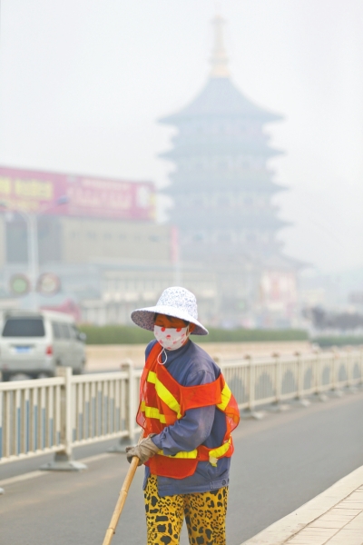 近日，在古都洛陽(yáng)，環(huán)衛(wèi)工人身后的“天堂”被霧霾籠罩著。