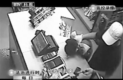 戴帽男子一手掐住加油站營業(yè)員，一手持發(fā)令槍指向另一營業(yè)員，要求“把錢給我裝起來”。