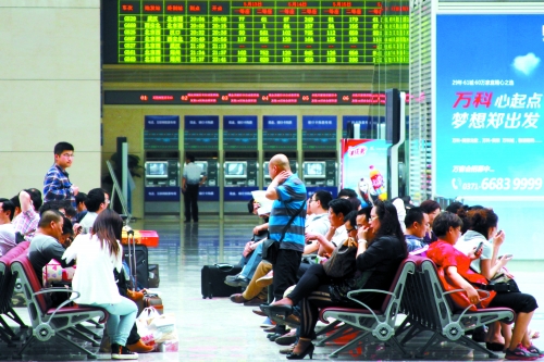 候車大廳溫度很高，一名乘客一手扇風(fēng)、一手擦汗