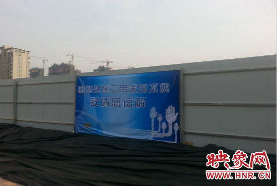 道路南側(cè)圍起了白色的圍擋，墻上標(biāo)示著“因地鐵施工帶來(lái)的不便敬請(qǐng)您諒解”的提示牌。