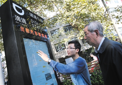 10月15日，滴滴工作人員（左）指導(dǎo)乘客使用“滴滴車站”的電子屏預(yù)約出租車。