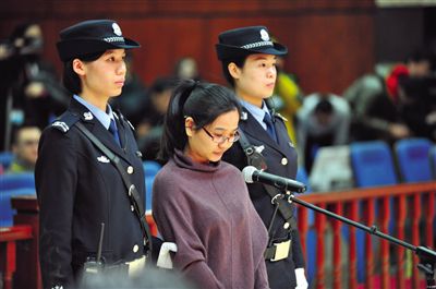 被告人盧梅低著頭，站在朝陽(yáng)法院刑事審判庭的被告席上。