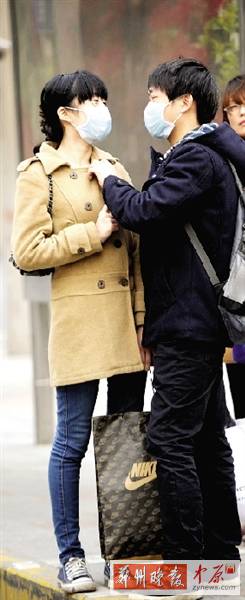 公交站臺(tái)上，一對(duì)年輕人戴著口罩，系緊衣領(lǐng)。